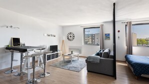 A modern living room with a sofa, a dining table, a TV, and a large window.