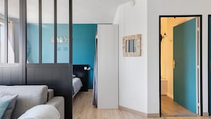 A modern room with a bed, a sofa, a door leading to another room, and a wall with a clock and a picture frame.