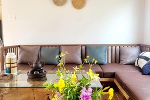 Een woonkamer met een glazen salontafel, een bank met meerdere kussens en een decoratieve wandversiering.
