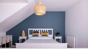 Et soveværelse med skråvægge, en seng med hvidgeng, et natbord og en hængende lampe.