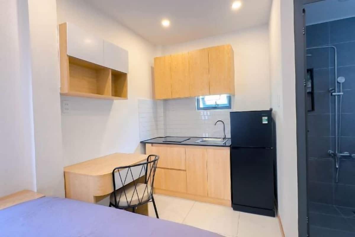 Une cuisine compacte avec des meubles en bois, un réfrigérateur noir et un petit coin repas équipé d’une chaise.