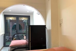 A narrow hallway with a black refrigerator, a pink chair, and a glass door leading to an outdoor area. - Lunaria Maison - Local Side (Ho Chi Minh City)