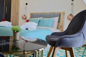 A hotel room with a bed, a chair, a small table with a plant, and a hanging light fixture. - Mi Casa Hotel Skopje (Skopje)