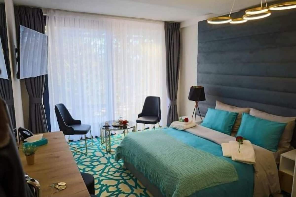 A hotel room with a bed, two chairs, a desk, a lamp, and a view of the outdoors.