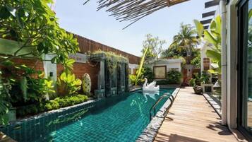 A swimming pool with a wooden deck, surrounded by lush greenery and a brick wall.
