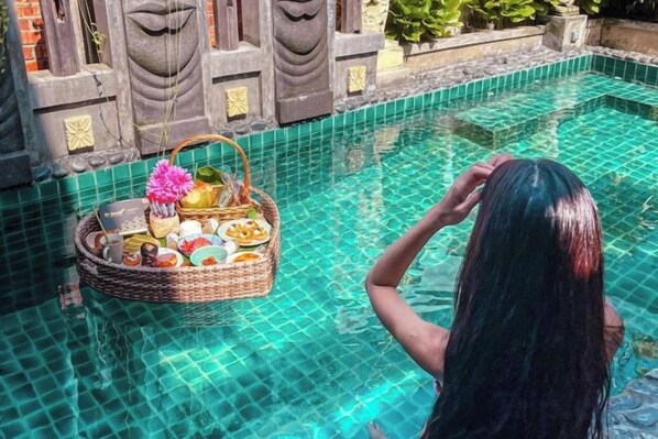 Una persona en una piscina con una cesta flotante que contiene comida y bebidas.