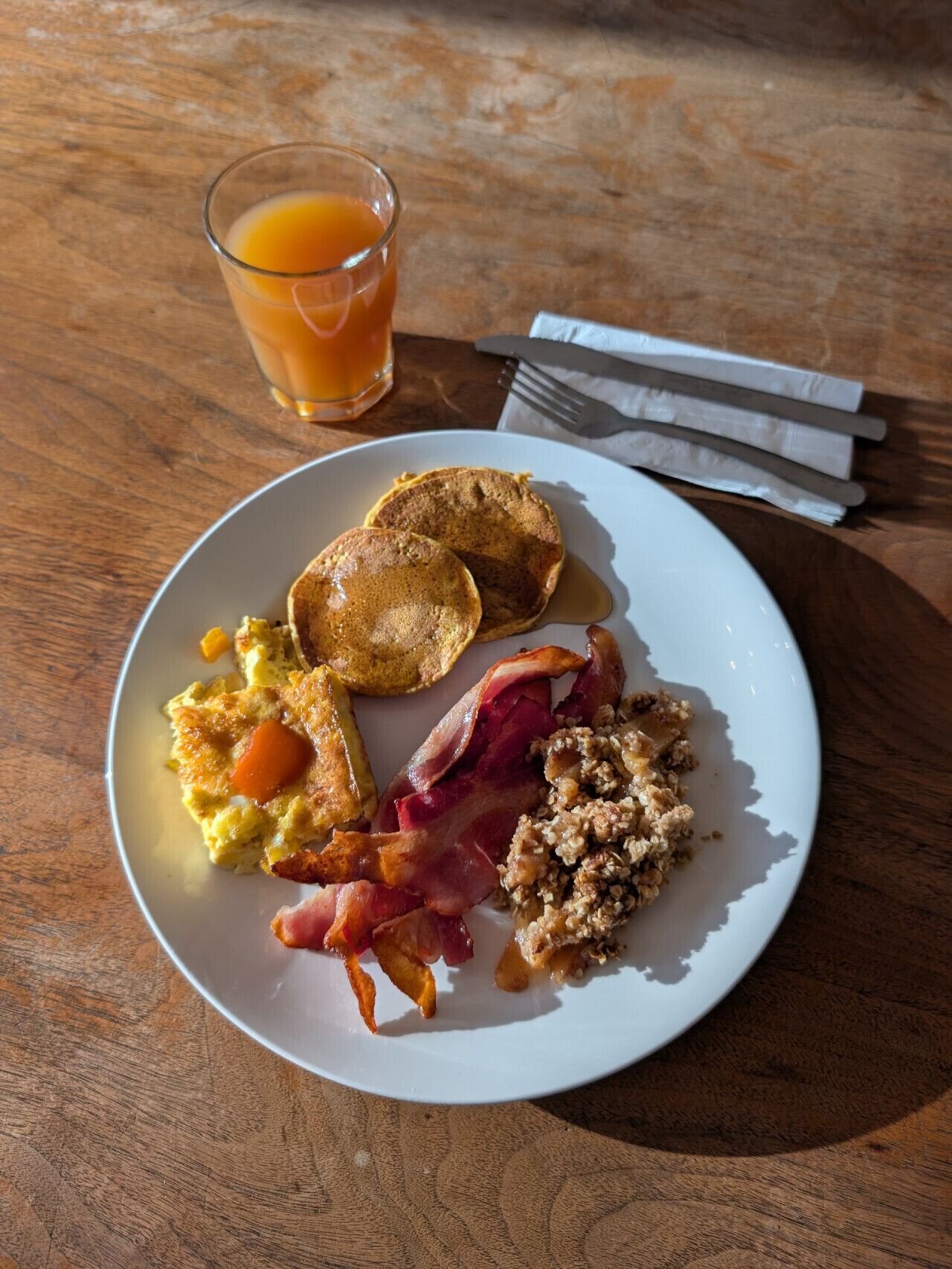 A breakfast plate with eggs, bacon, and toast on a wooden table.