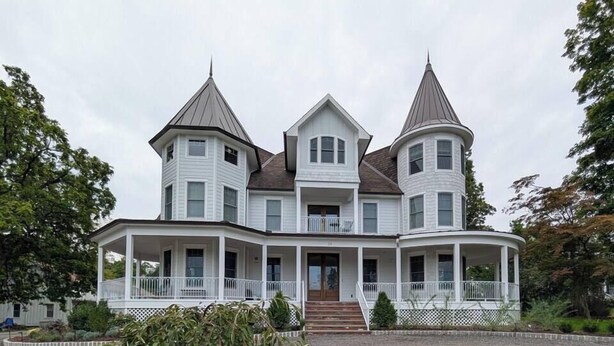 A large, white, multi-story house with a symmetrical design, featuring a central entrance and two side wings.