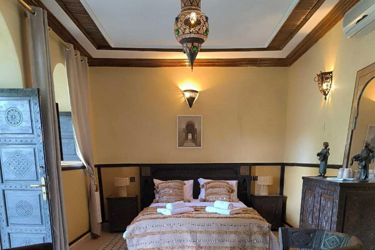Ein Hotelzimmer mit einem großen Bett, zwei Sesseln, einem kleinen Tisch, einer Zierdebeleuchtung an der Decke und einer Wandlampe.