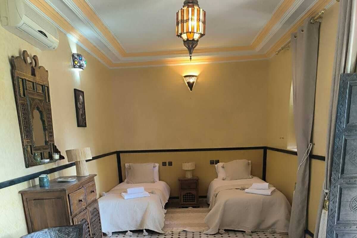 Ein Hotelzimmer mit zwei Betten, einem Holzstuhl, einem kleinen Tisch und einem dekorativen Spiegel.