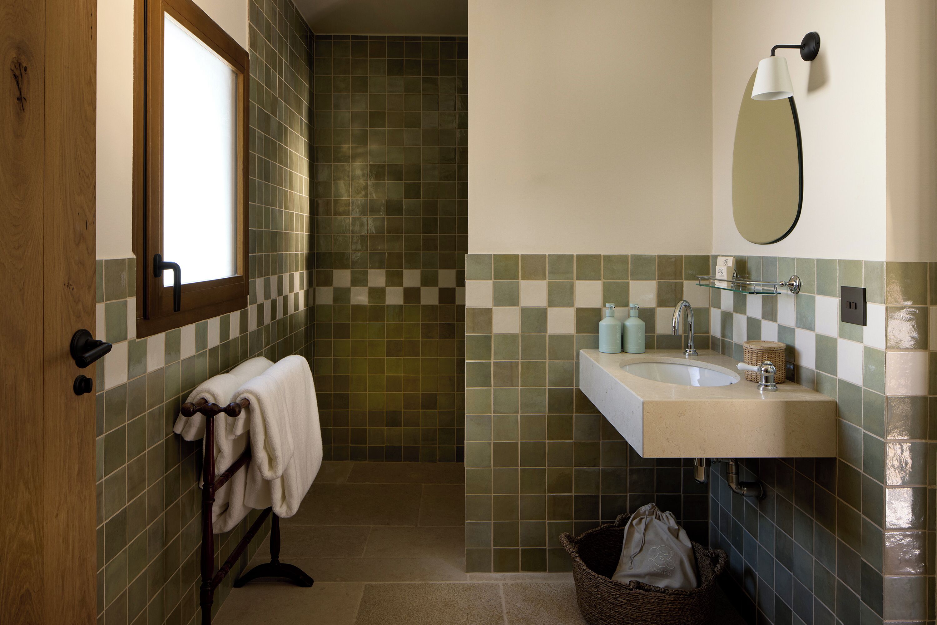 A bathroom with a wooden door, a towel rack, a sink with a mirror, and a tiled shower area.