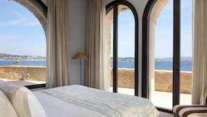 A bedroom with a large bed, a lamp, and a view of the sea through arched windows. - Zannier Île de Bendor (Bandol)