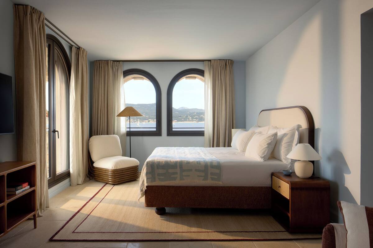 A bedroom with a bed, a chair, a nightstand, a lamp, and a TV.