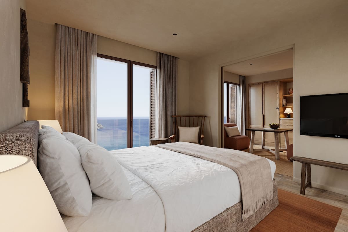 A hotel room with a large bed, a TV, a desk, and a view of the ocean.