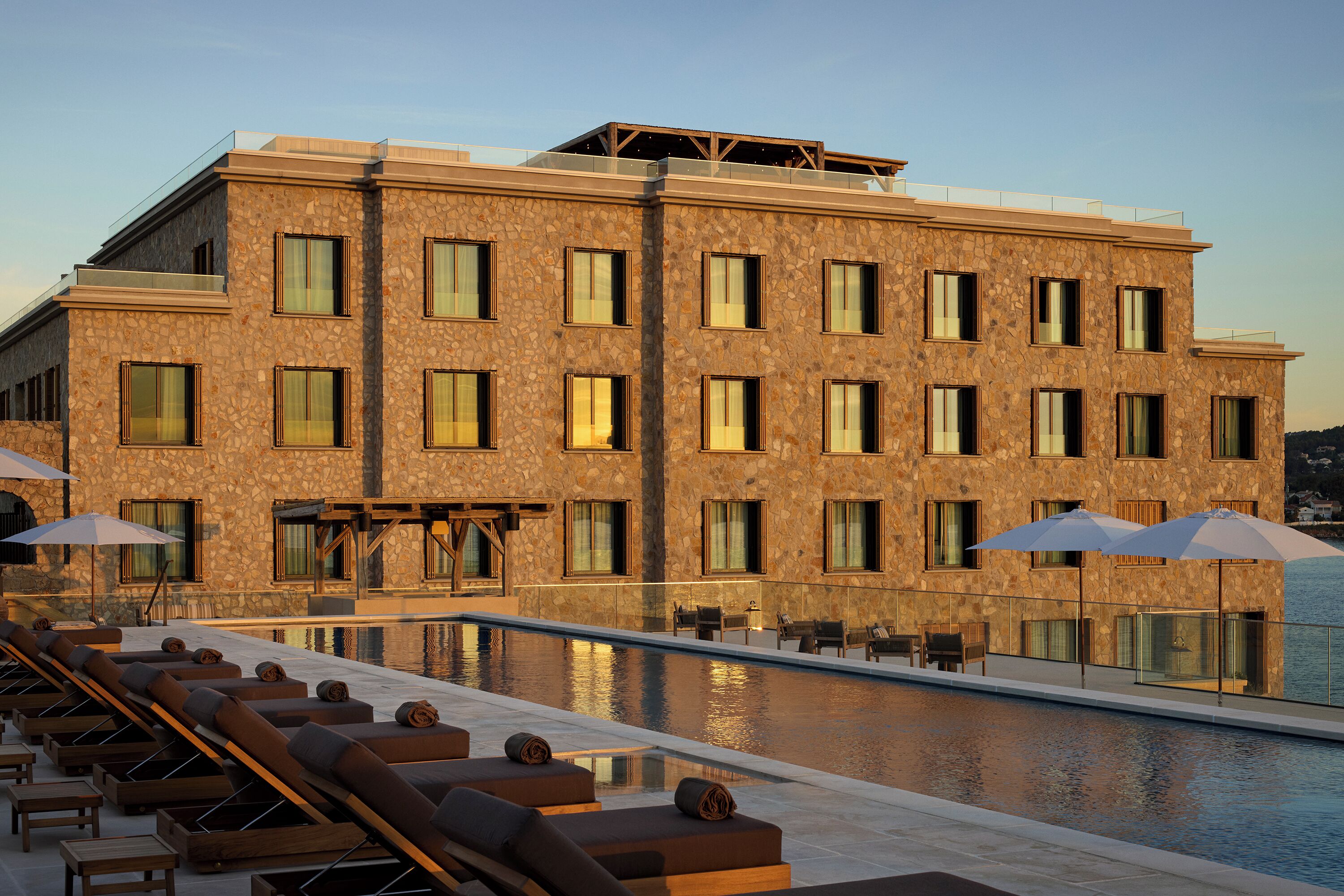 Un hotel moderno con piscina, tumbonas y fachada de piedra.