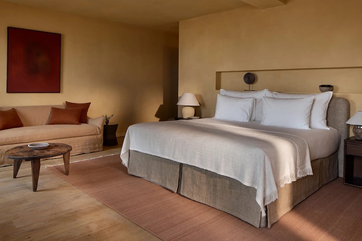 A bedroom with a bed, a sofa, a small table, and a lamp.