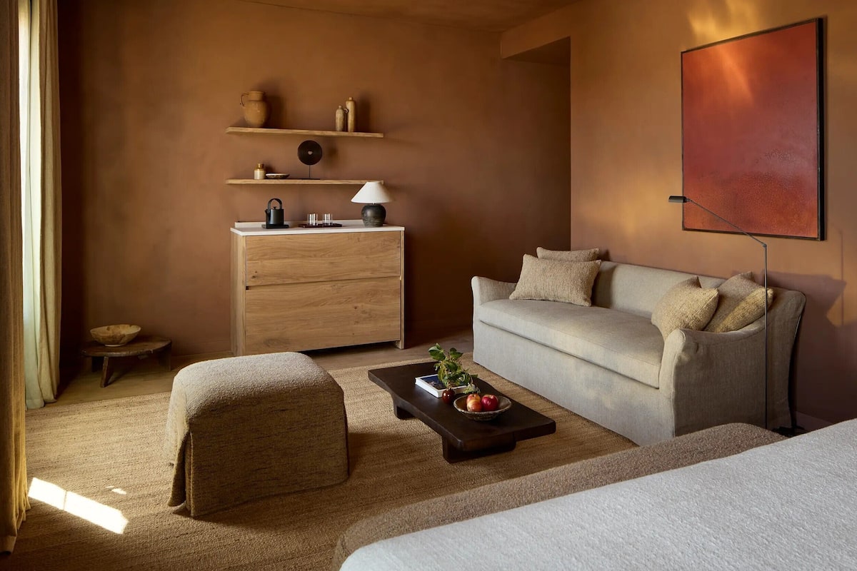 A modern room with a sofa, a wooden dresser, a coffee table with fruits, a lamp, and a wall-mounted artwork.