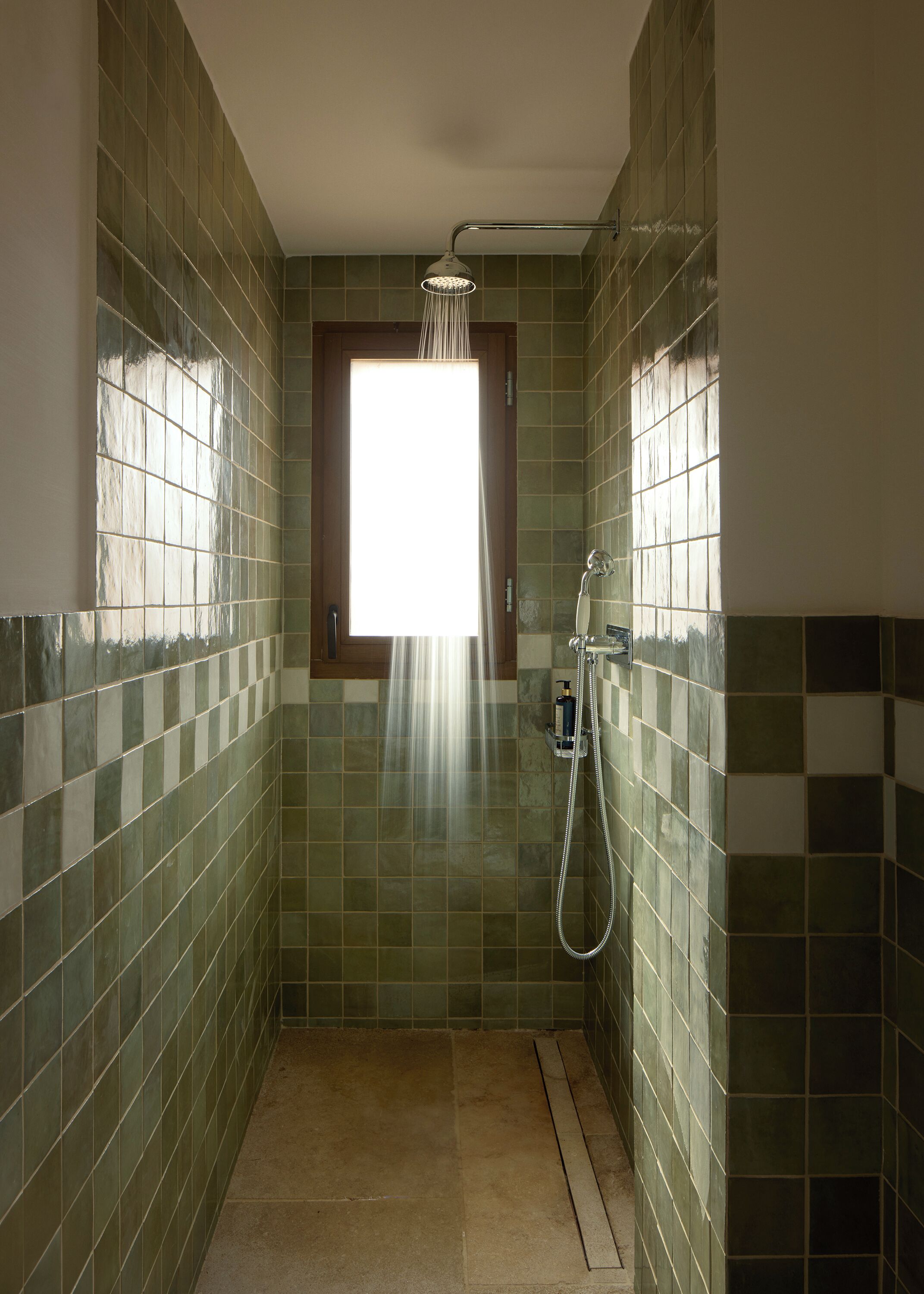 A narrow shower area with a window, tiled walls, and a handheld showerhead.