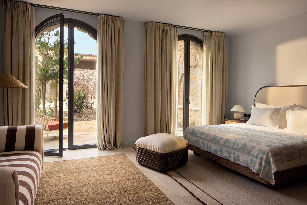 A bedroom with a bed, a chair, a nightstand, and a window with curtains.