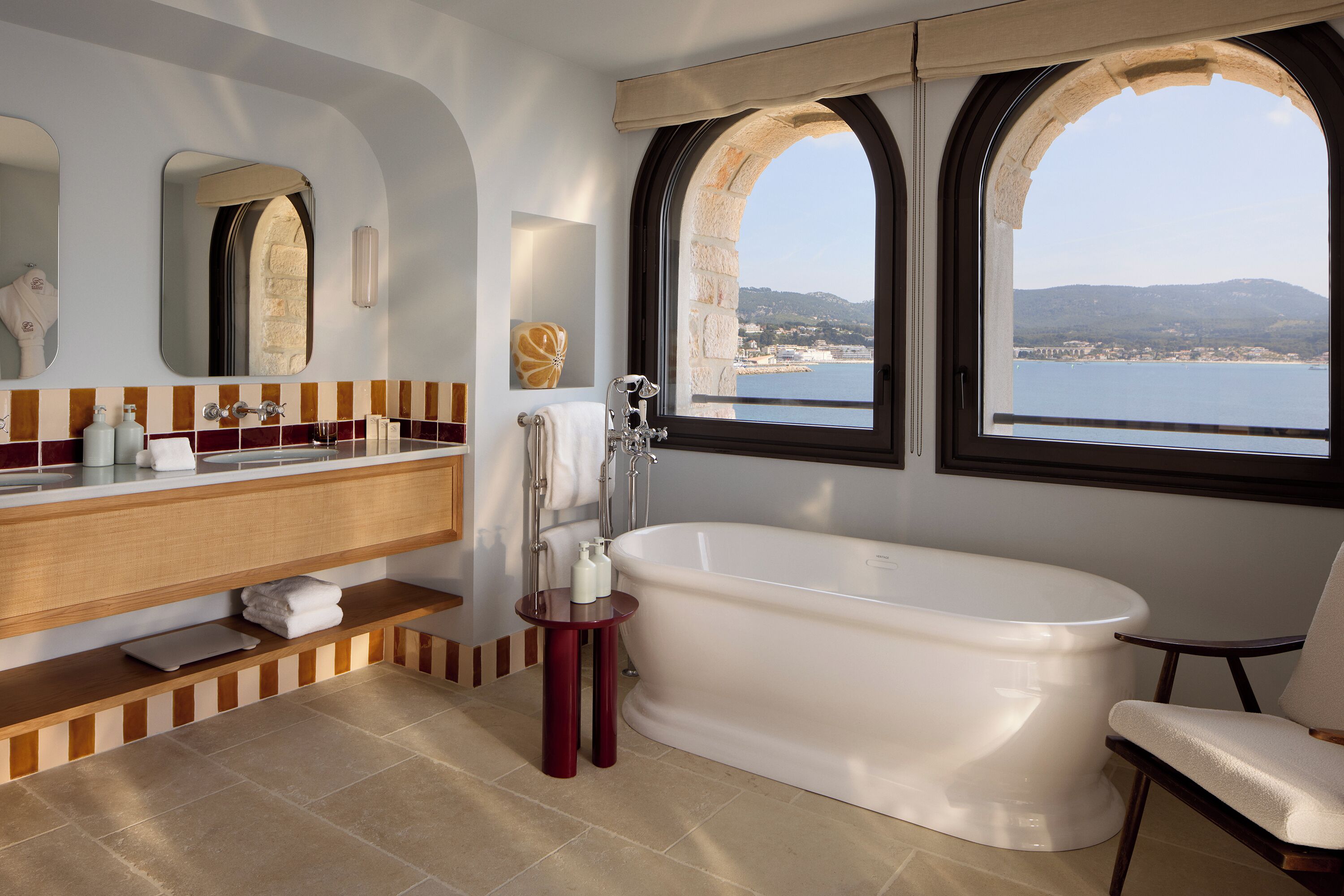 A bathroom with a bathtub, a vanity with a mirror, and a view of the sea.