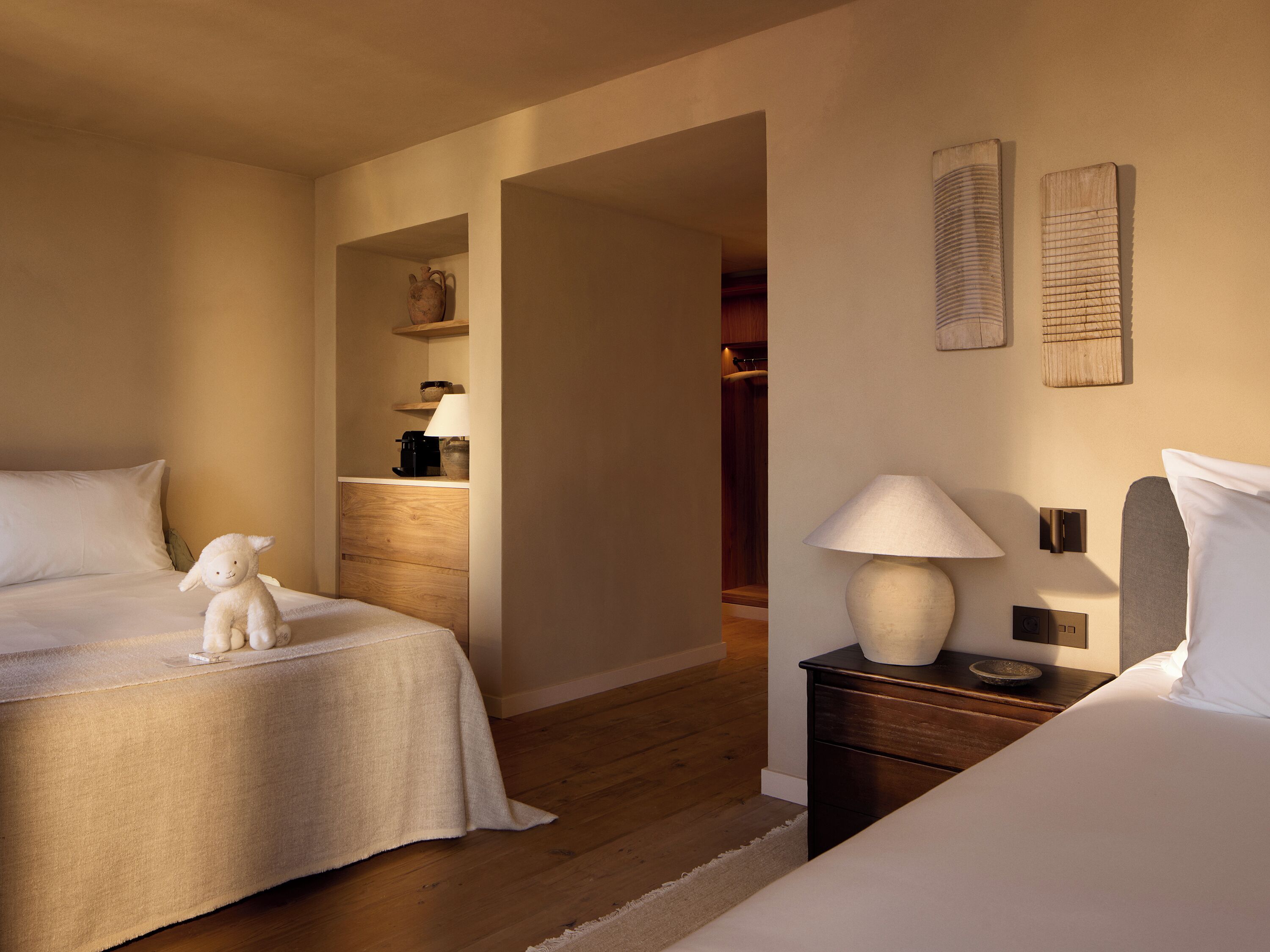 Una habitación de hotel con dos camas, una mesita de noche con lámpara, una pequeña mesa con lámpara y un estante con cafetera.