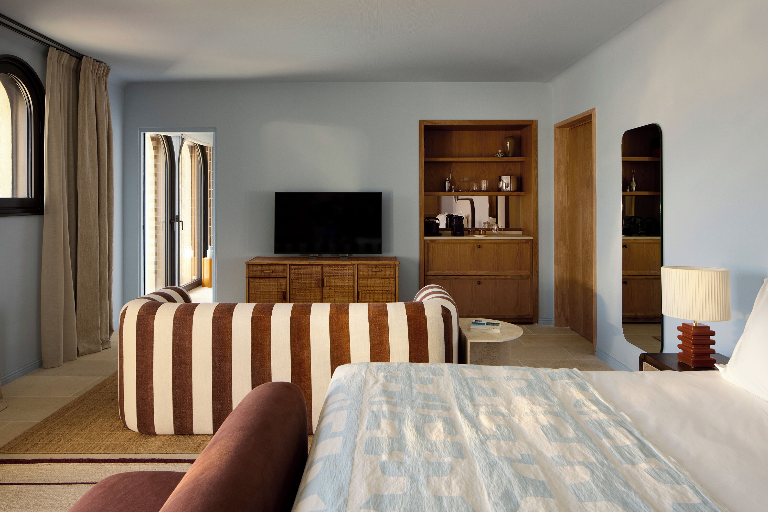A hotel room with a bed, a sofa, a television, a wooden cabinet, and a small table.