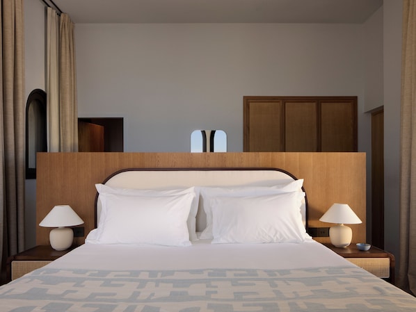 A hotel room with a large bed, two bedside lamps, a wooden headboard, and a view of the city through a window.