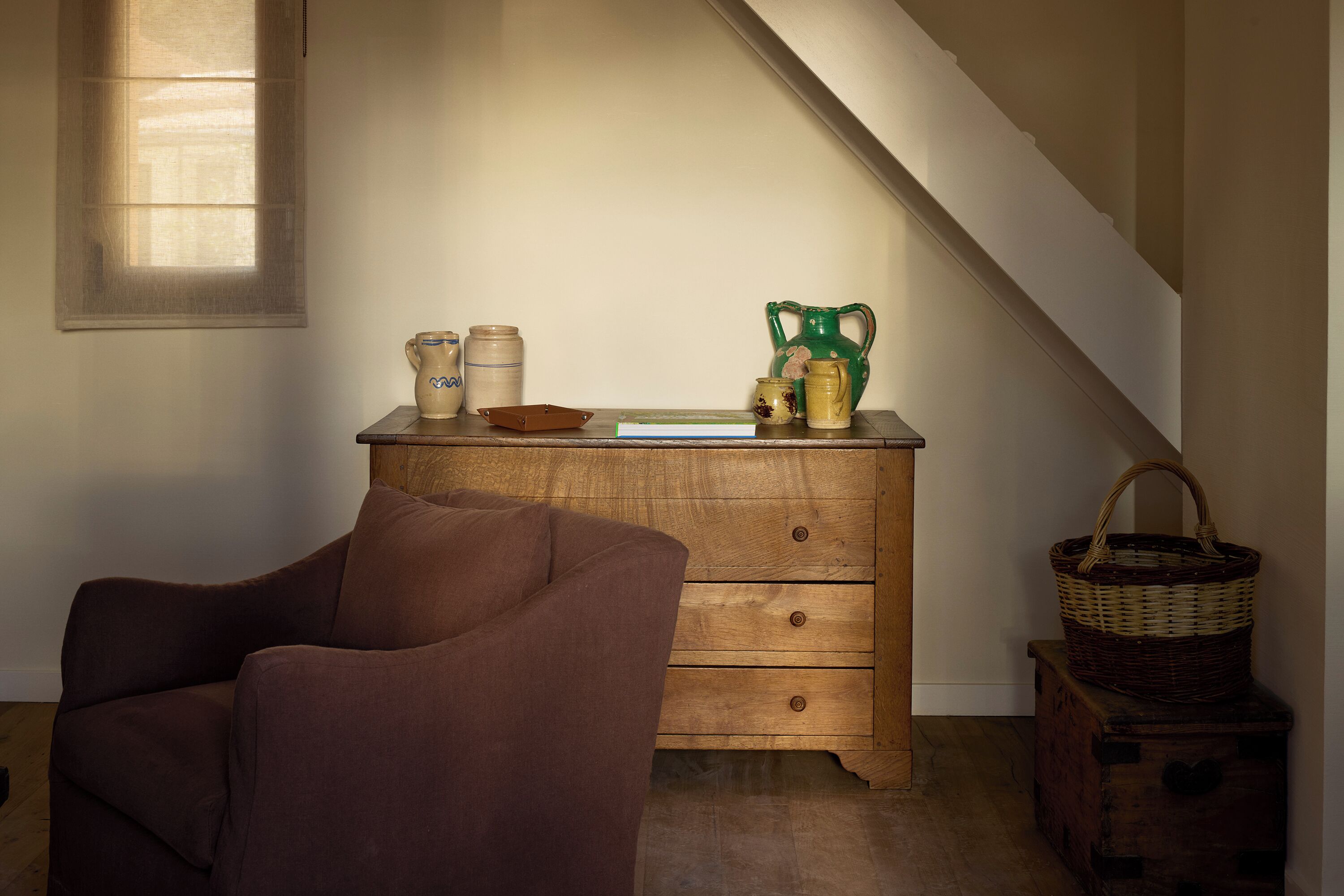 A room with a wooden dresser, a brown chair, and a window with natural light.