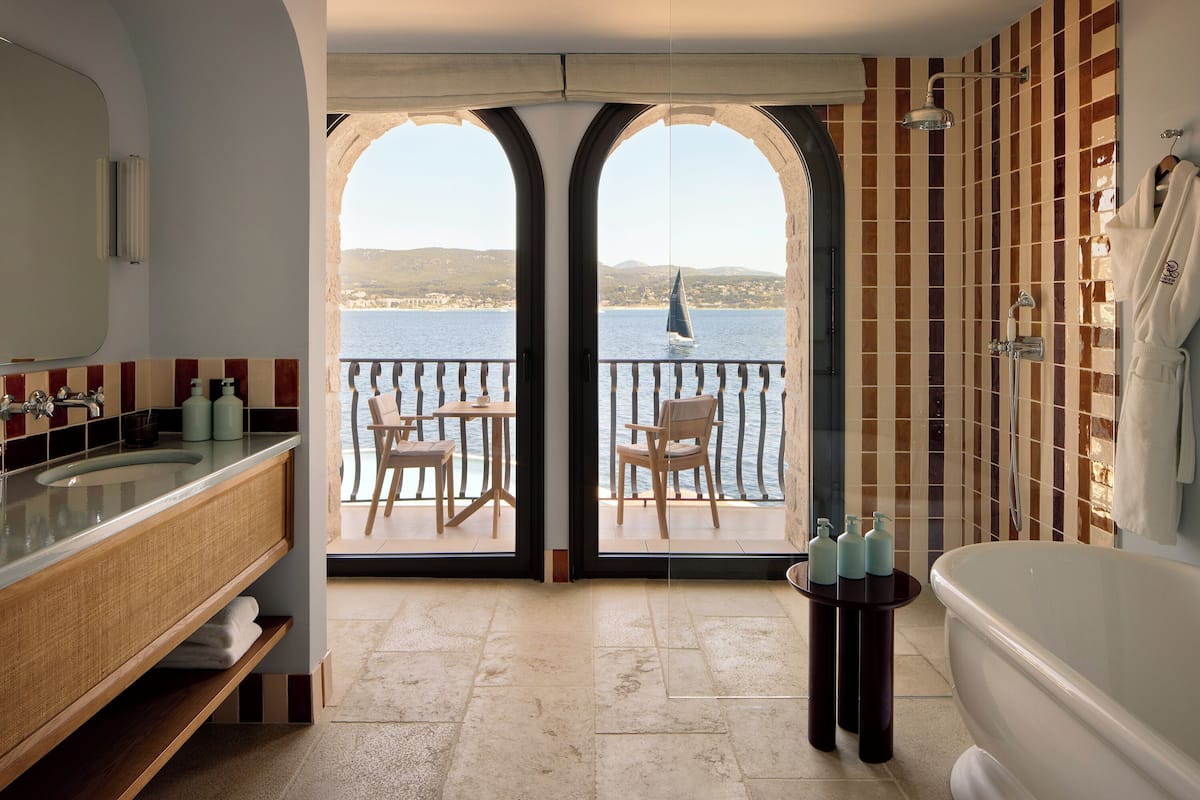 A bathroom with a bathtub, a sink, and a mirror. There is a view of the sea through an arched doorway.