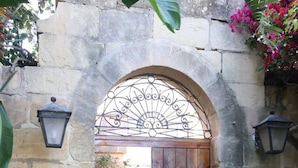 Un arco in pietra conduce a una porta di legno, circondato da vasi di piante e un piccolo prato.