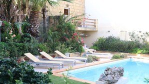 Area piscina con lettini, una roccia decorativa e vegetazione rigogliosa.