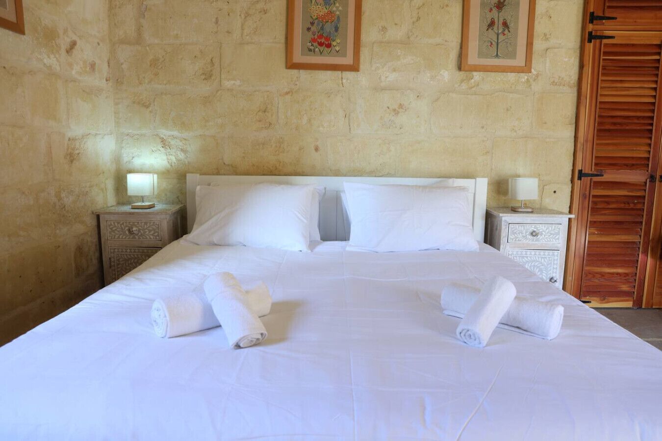 A neatly made bed with white linens and towels, two bedside tables with lamps, and a wooden door.