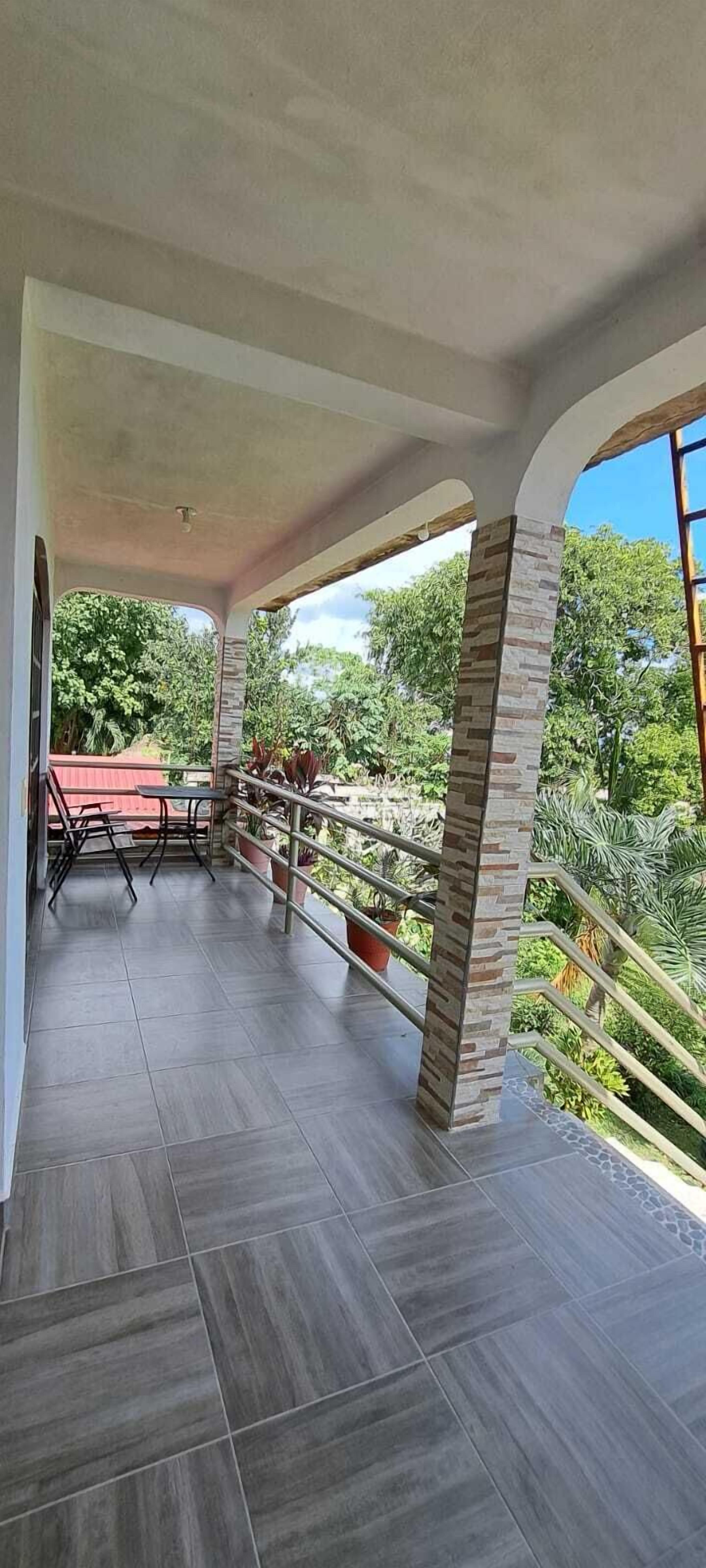 Ein überdachter Balkon mit Blick auf Grünflächen, einem Tisch und Stühlen.