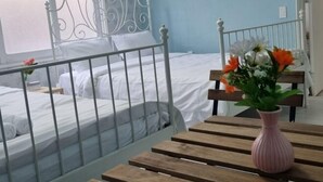 A room with a bed, a white metal headboard, a wooden table with a pink vase, and a window with a view.