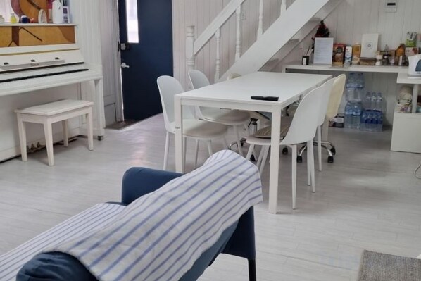 Una habitación con un piano, una mesa de comedor con sillas, un banco y una escalera.