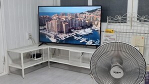 A television displaying a coastal cityscape, a white TV stand, and a standing fan.