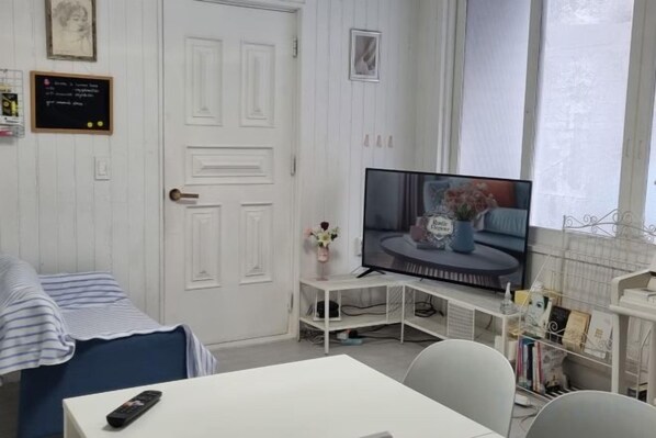 A room with a bed, a TV on a stand, a small table, and a chair.