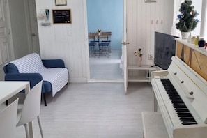 Een kamer met een piano, een bank, een eettafel en een televisie.
