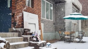 A snowy outdoor area with steps leading up to a building, a table with chairs, and a green umbrella.