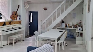 A room with a piano, a dining table with chairs, a staircase, and a door leading to another room.