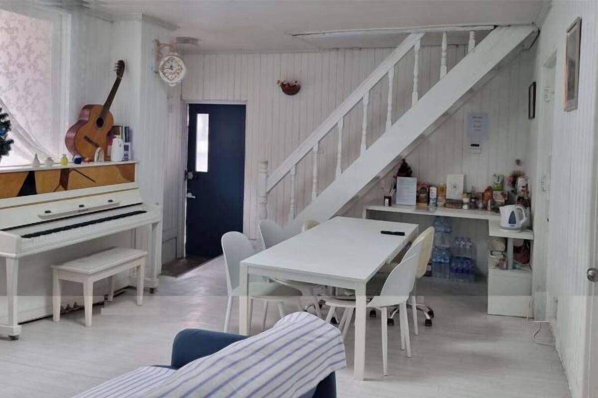 A room with a piano, a dining table with chairs, a staircase, and a door leading to another room.