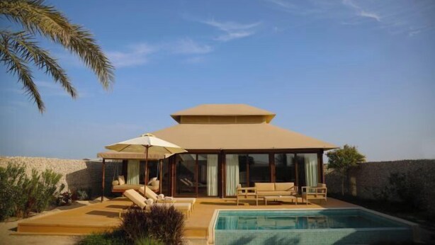 A modern villa with a swimming pool, outdoor seating, and a view of the desert landscape. - The Outpost Al Barari Camp (Al Wakrah)