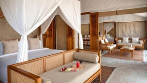 A bedroom with a canopy bed, a sitting area with a sofa and chairs, and a dining table with a plate of fruit. - The Outpost Al Barari Camp (Al Wakrah)