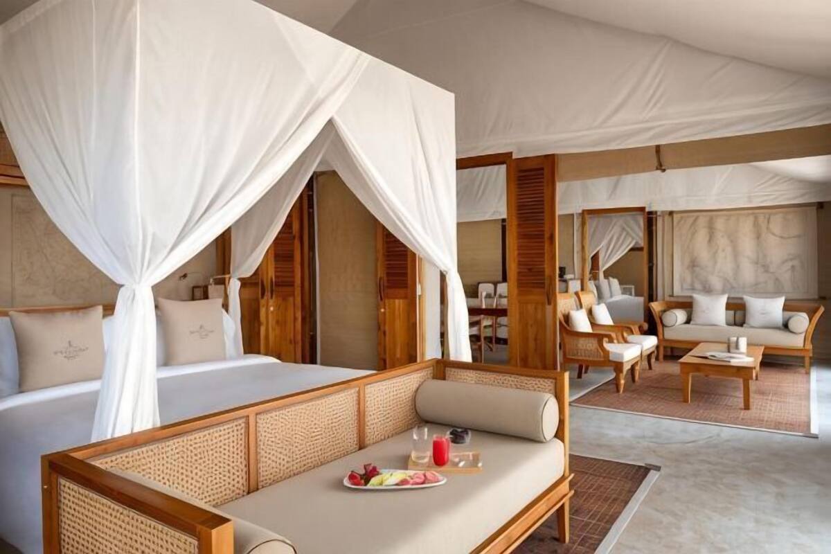 A bedroom with a canopy bed, a sitting area with a sofa and chairs, and a dining table with a plate of fruit.