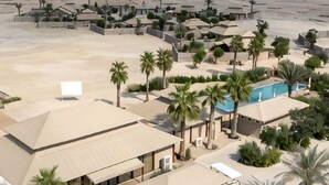 An aerial view of a resort with multiple buildings, palm trees, and a swimming pool. - The Outpost Al Barari Camp (Al Wakrah)
