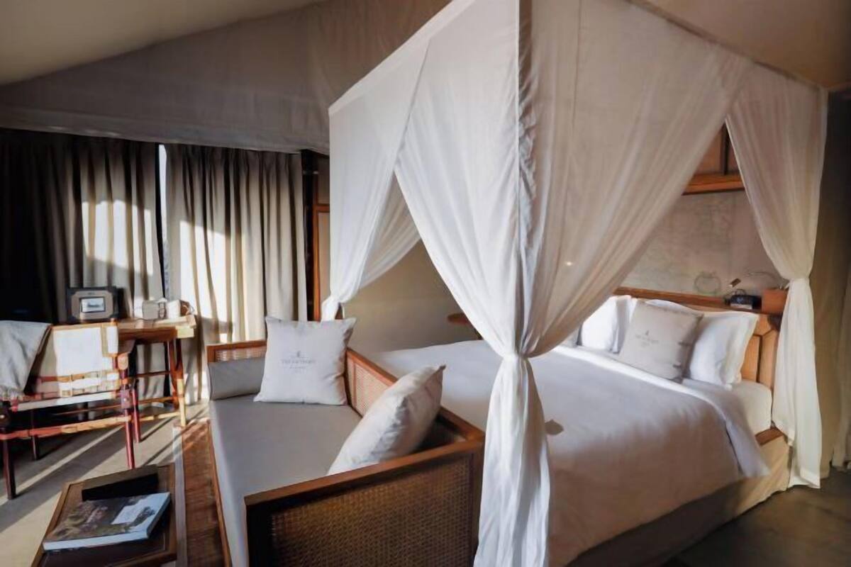 A bedroom with a canopy bed, a sofa, a small table, and a TV.