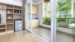 A modern kitchen with built-in appliances, a dining area with a table and chairs, and a large sliding glass door leading to a balcony with a view of greenery. - Cozrum Homes - Yoga Corner (Ho Chi Minh City)