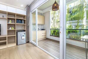 A modern kitchen with built-in appliances, a dining area with a table and chairs, and a large sliding glass door leading to a balcony with a view of greenery. - Cozrum Homes - Yoga Corner (Ho Chi Minh City)