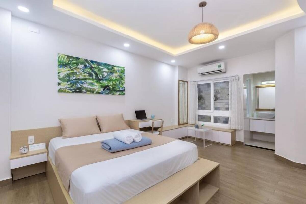 Une chambre d’hôtel moderne, dotée d’un grand lit, d’un bureau, d’une chaise, d’une fenêtre avec des rideaux et d’un tableau au mur.
