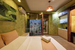 Ein Zimmer mit Bett, einer Glastür zum Balkon, einer Küchenzeile und einer Wand mit einem abstrakten Grünmuster.